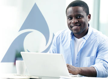 Man in a light blue shirt smiles while working on a laptop, with a stylized blue geometric logo in the background.