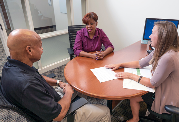 Three people sit around a conference table in an office, discussing paperwork in front of them.