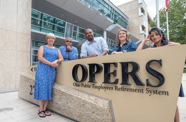 Five people stand and lean on the large OPERS sign outside the Ohio Public Employees Retirement System building.
