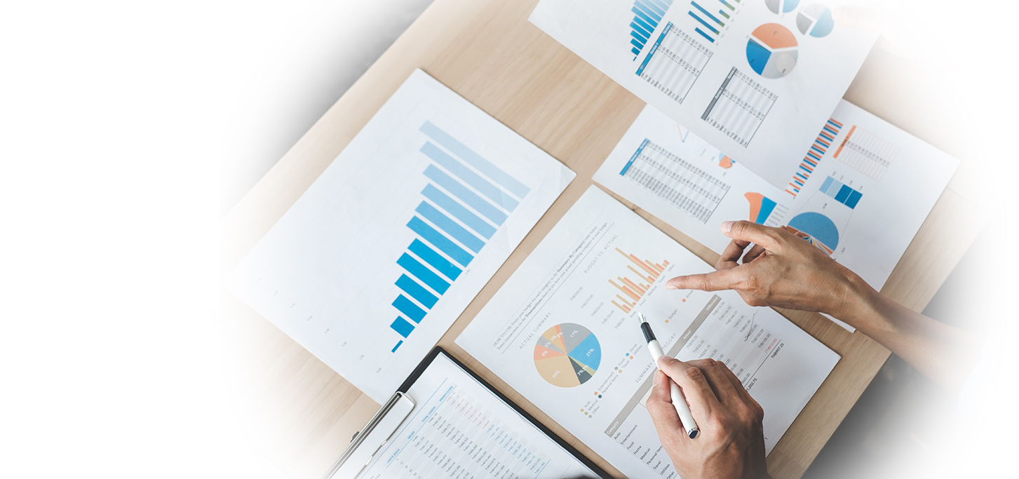 Two people review printed financial charts and graphs on a desk, analyzing bar graphs, pie charts, and data tables with pens.