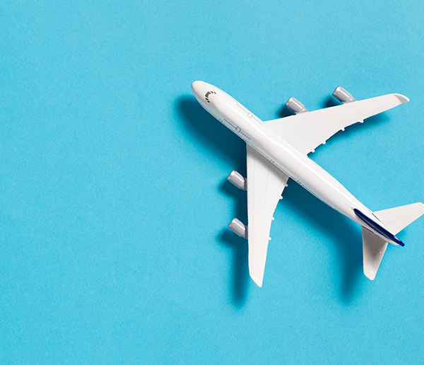 A white toy airplane with blue accents is positioned diagonally on a solid light blue background.